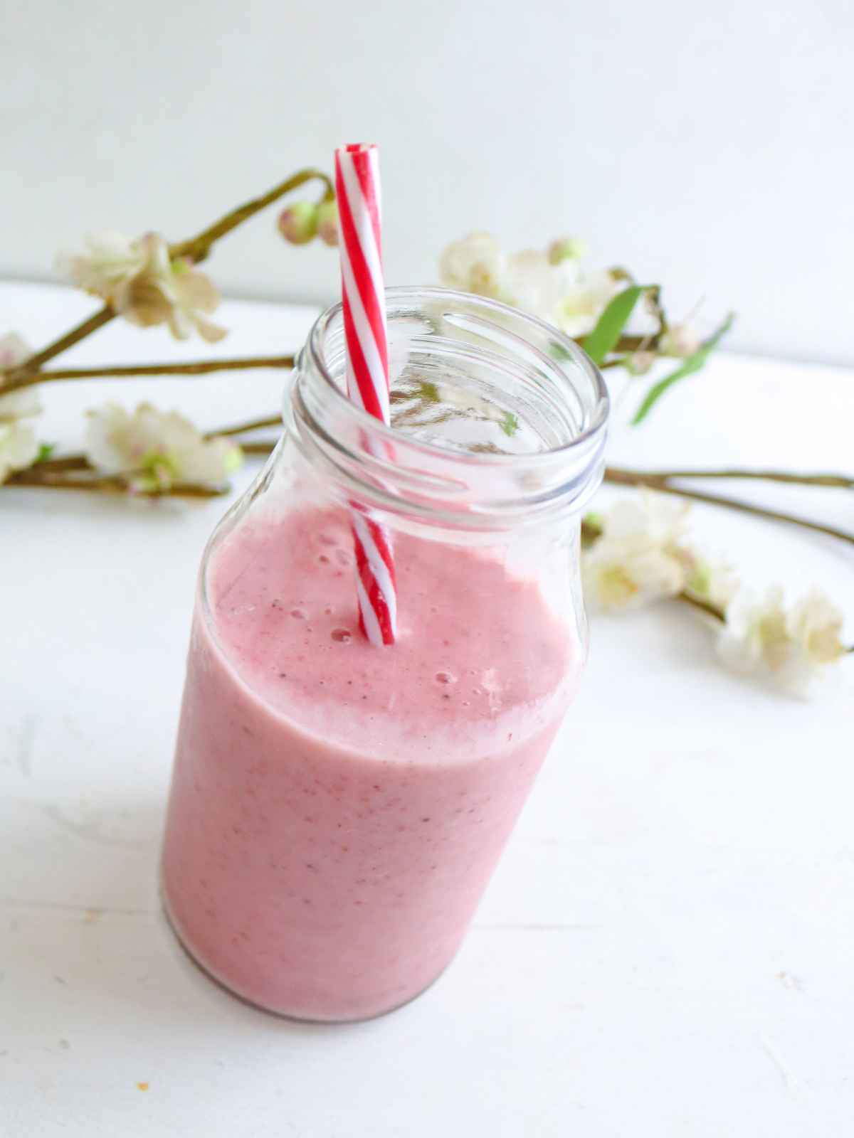 pink color smoothie in a glass jar with white and red striped straw. 