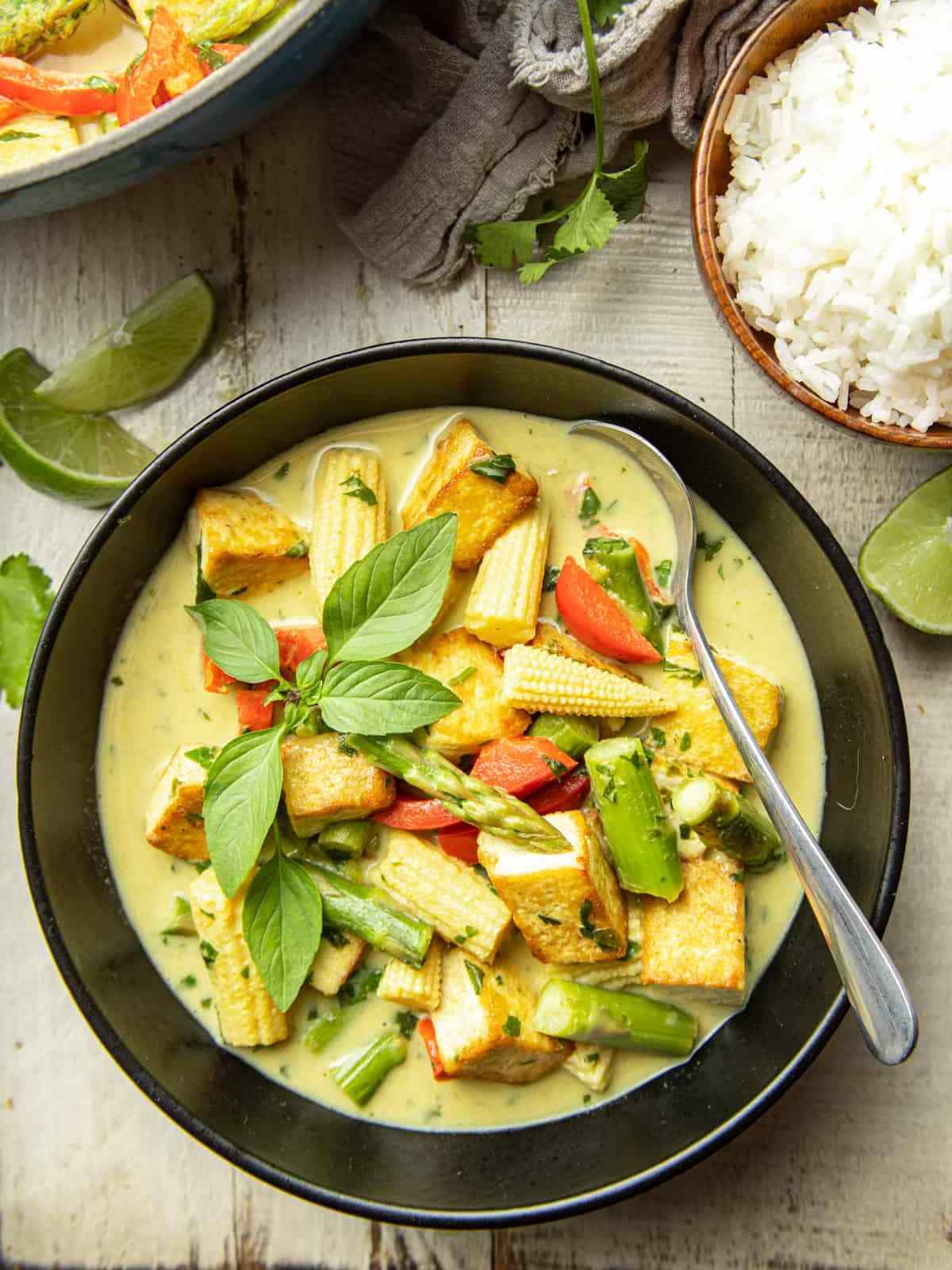 Black color bowl filled with Thai green tofu curry, basil leaf on top.