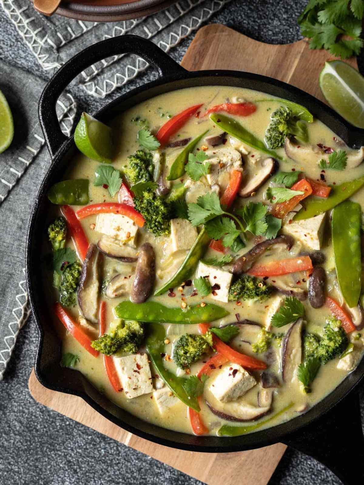 Green color tofu curry with red bell peppers and green peas served in a cast iron pan.