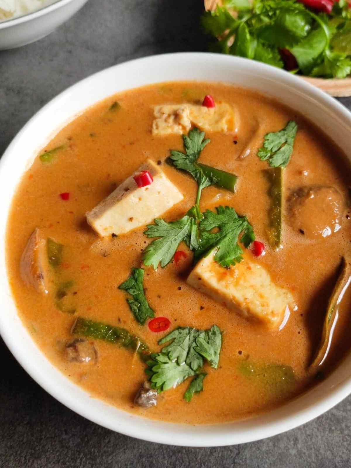 Curry served in a white color bowl featuring tofu and veggies and creamy orange color curry.