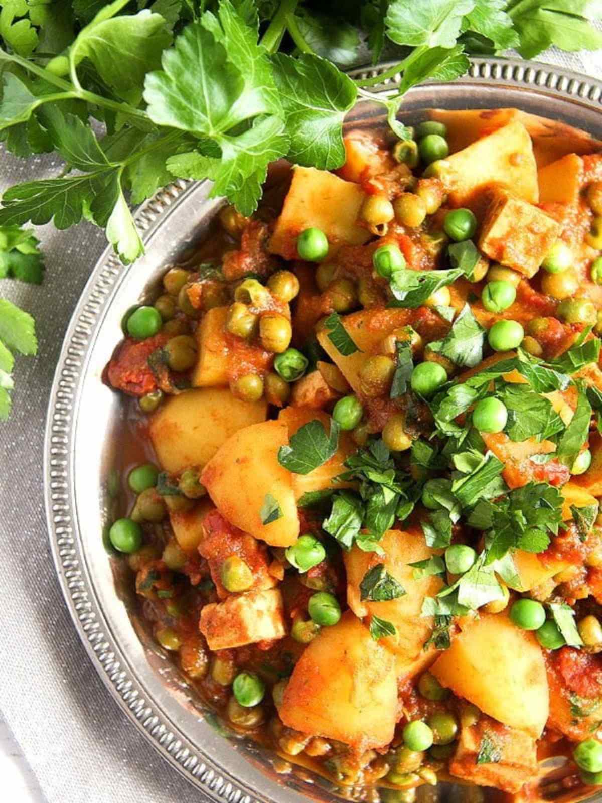 Silver round dish filled with tofu potatoes and peas curry.