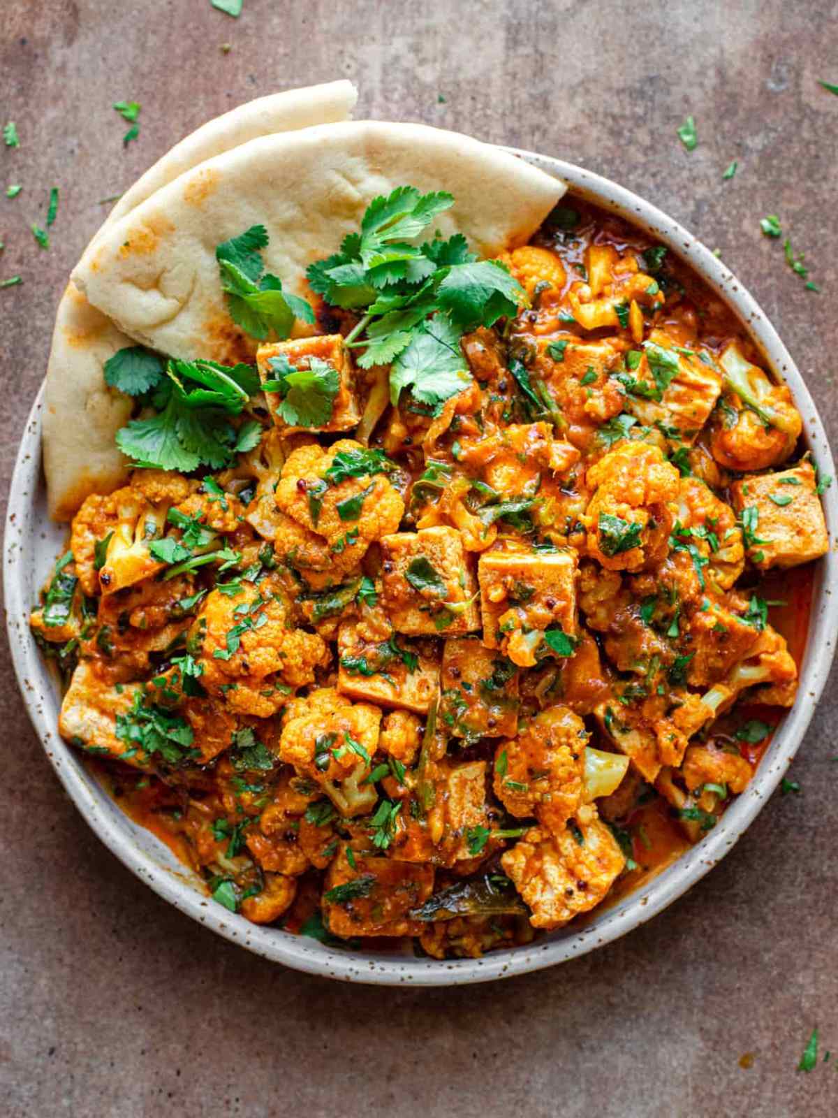 Orange color Tofu curry topped with cilantro leaves and served with naan.