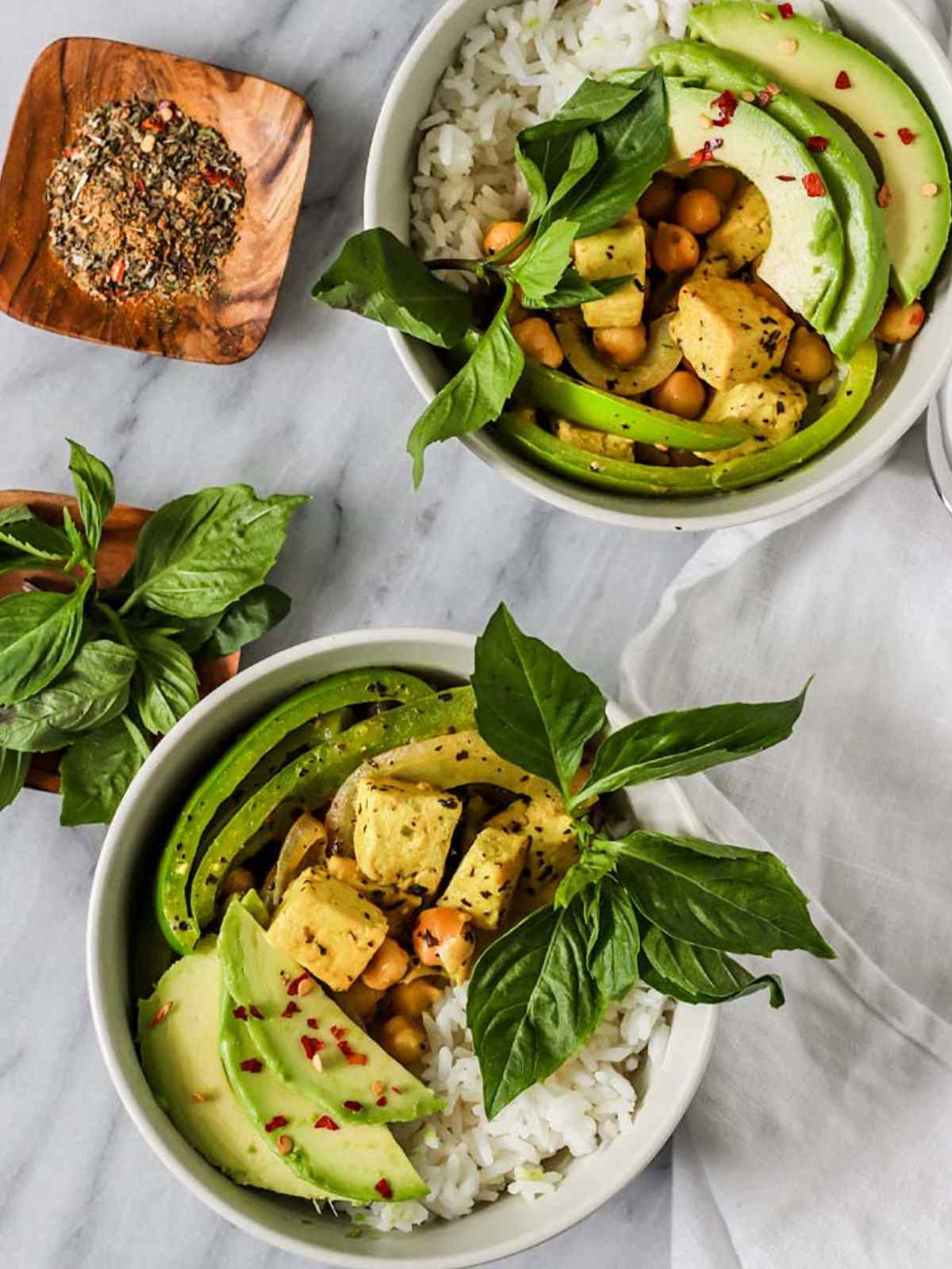 Two bowl of Thai tofu curry topped with avocado and basil leaves.