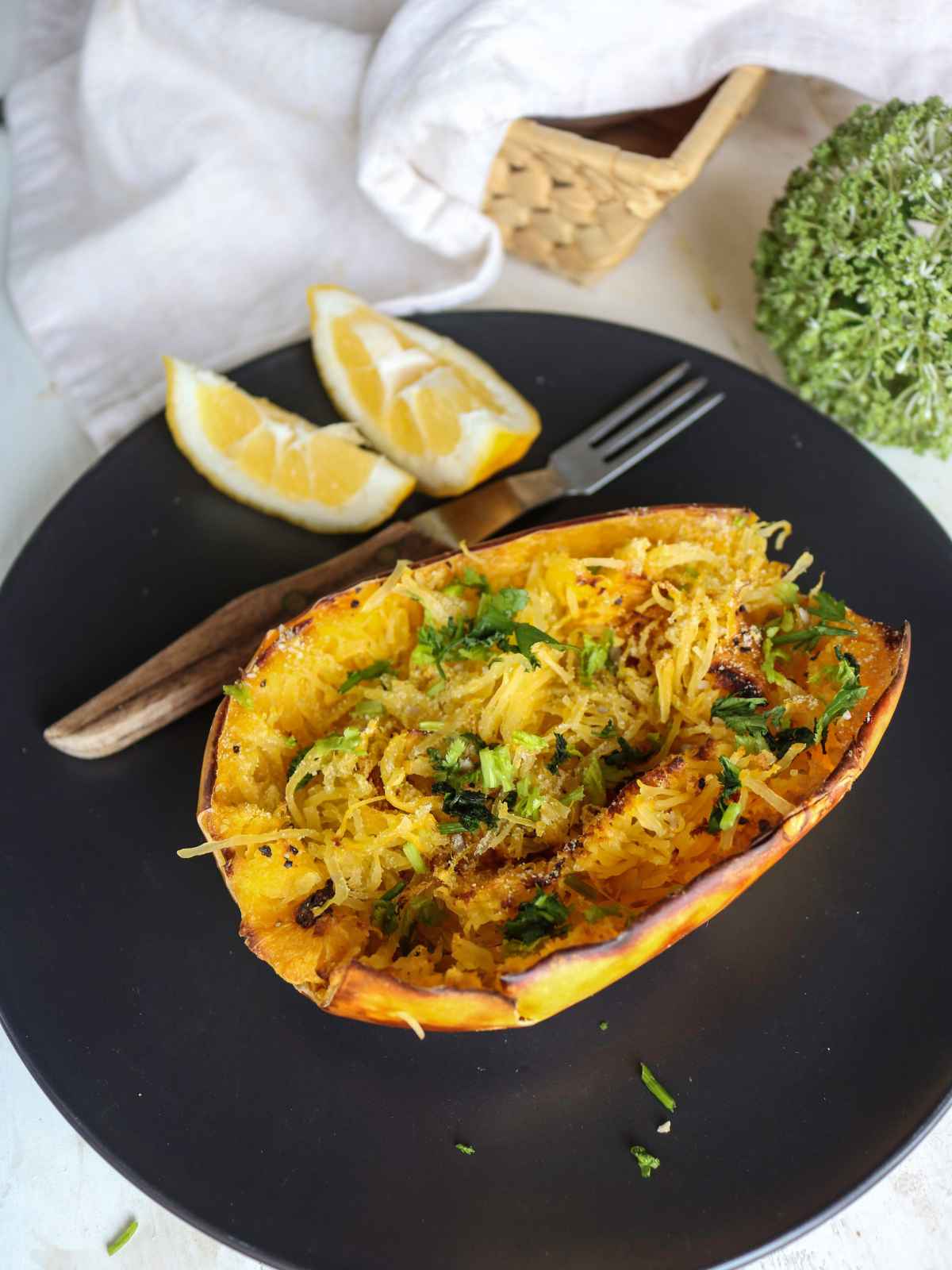 spaghetti squash served in a black plate and lemon wedges on side, topped with green herbs.