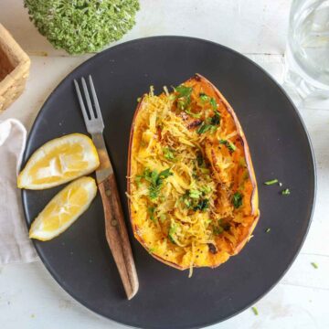 air fryer spaghetti squash served in a black plate, fork and lemon slices on side.