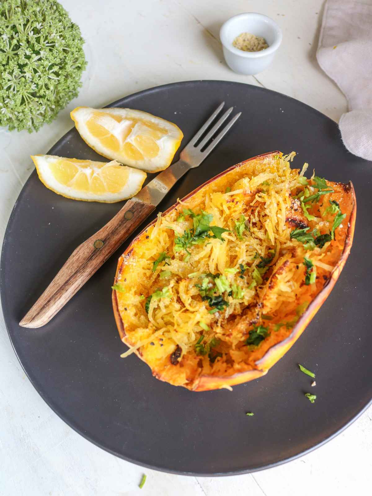 air fryer spaghetti squash served in a black plate with fork and lemon wedges.