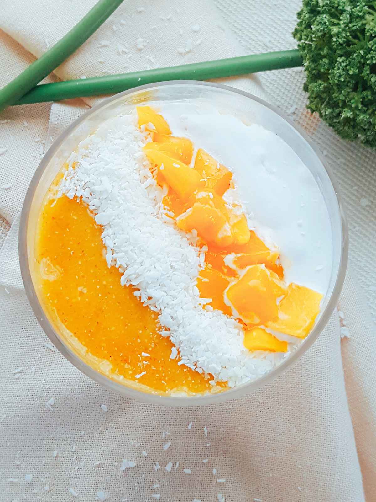 Semolina pudding served in a glass jar topped with coconut cream, mango slices and coconut shreds.