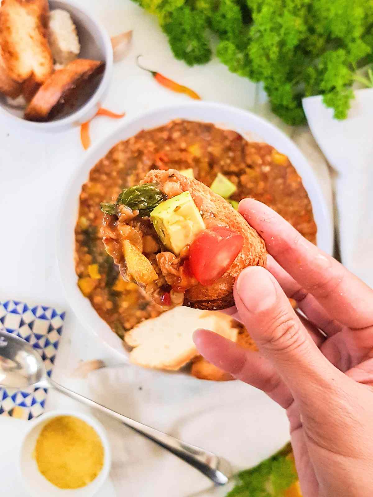 holding piece of crusty bread topped with lentil spinach stew.