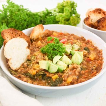 Lentil Spinach stew served in a bowl topped with fresh parsley, avocado slices and crusty bread.