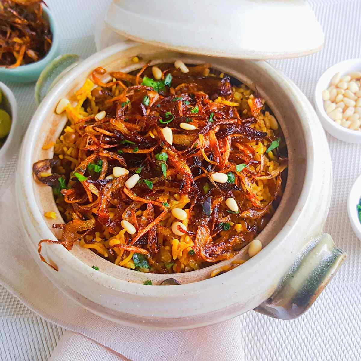 Mujadara served in a bowl with lid , green olives, pine nuts and cilantro on background.