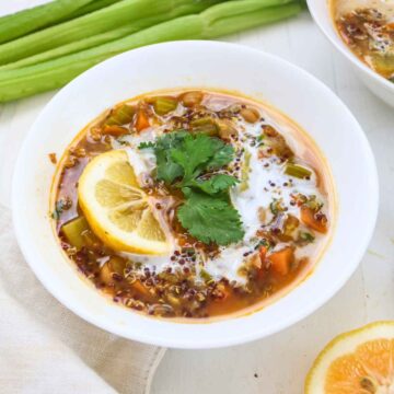Quinoa and chickpea stew served in a white bowl garnished with lemon wedges and cilantro leaves.
