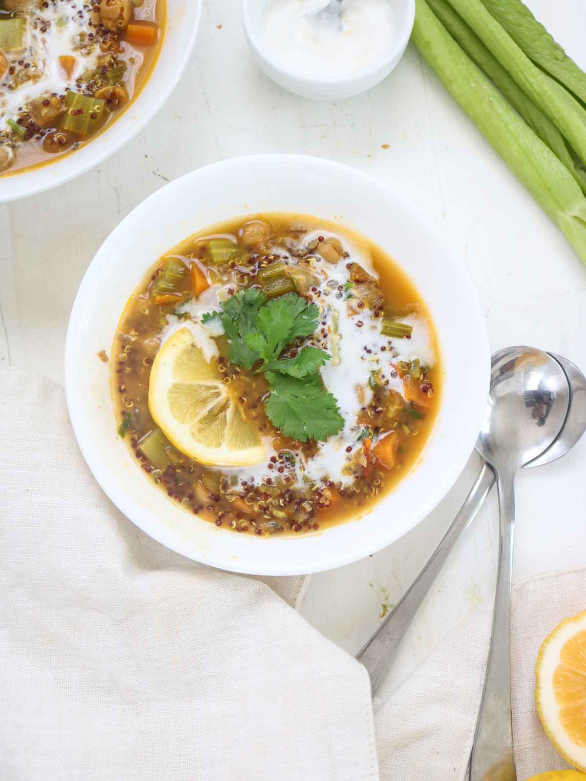 Stew served in a white bowl garnished with lemon wedges and cilantro leaves. metal spoons and celery stalk in background.