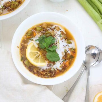 Quinoa and chickpea stew served in a white bowl garnished with lemon wedges and cilantro leaves.