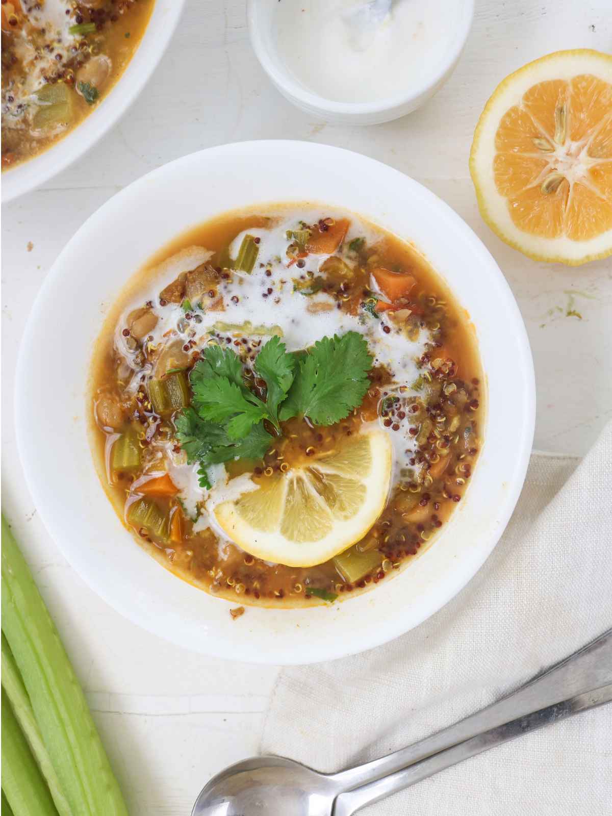 Quinoa and Chickpea Stew served in white bowl garnished with lemon wedge and green cilantro leaves.