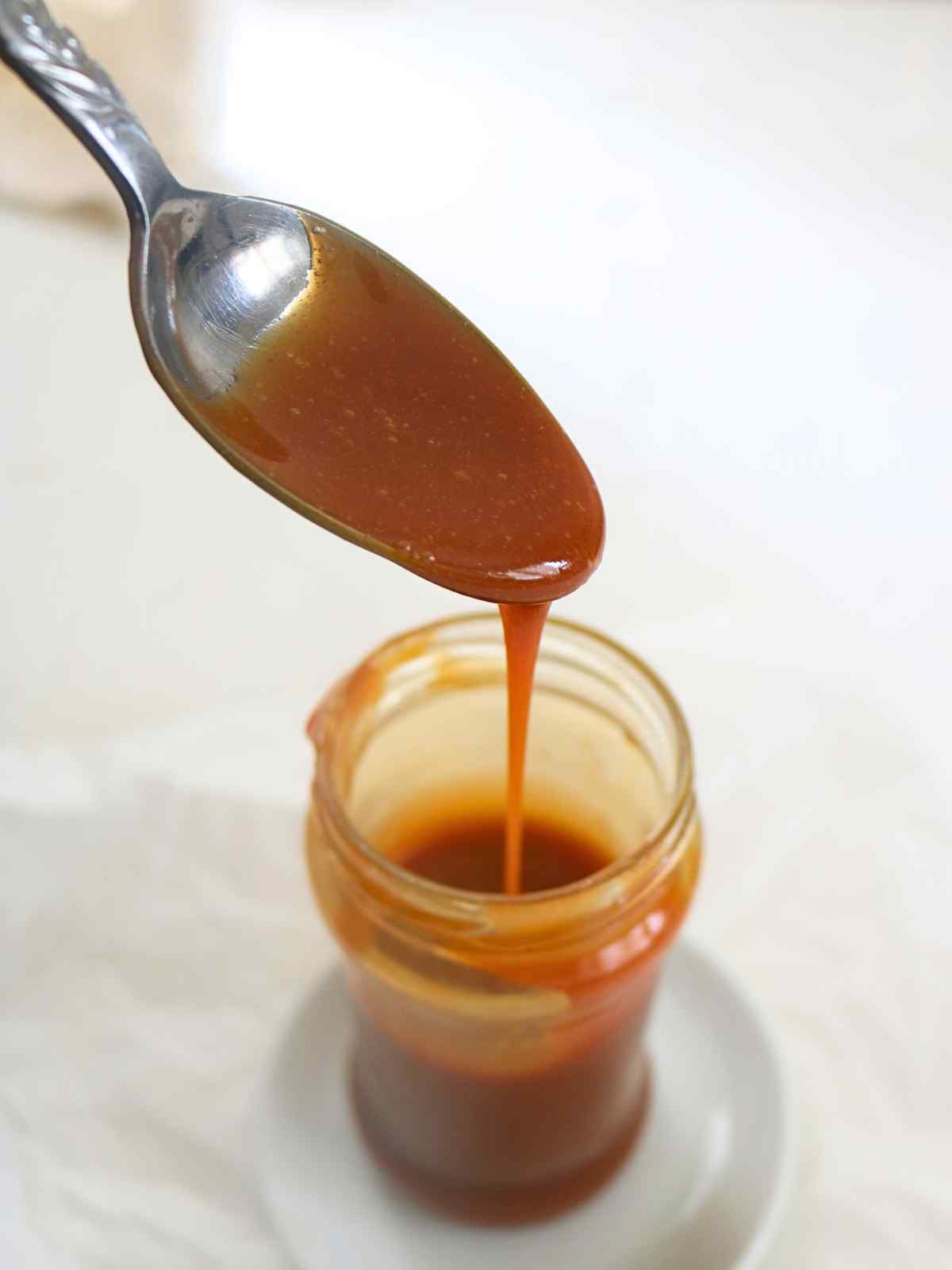 Pouring salted caramel sauce with a spoon in glass jar.