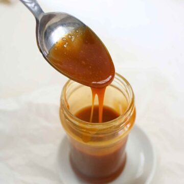 Pouring vegan salted caramel with a spoon in a glass jar.