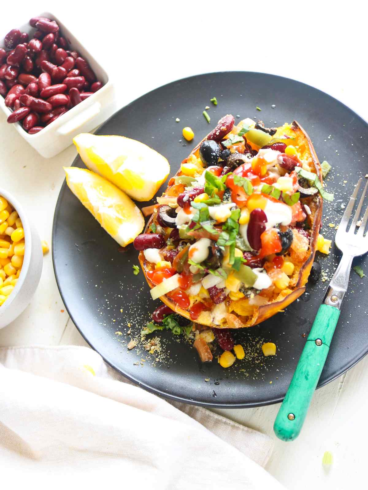 Stuffed Spaghetti Squash Served on a black plate and fork, lemon wedges and red beans placed in the background.