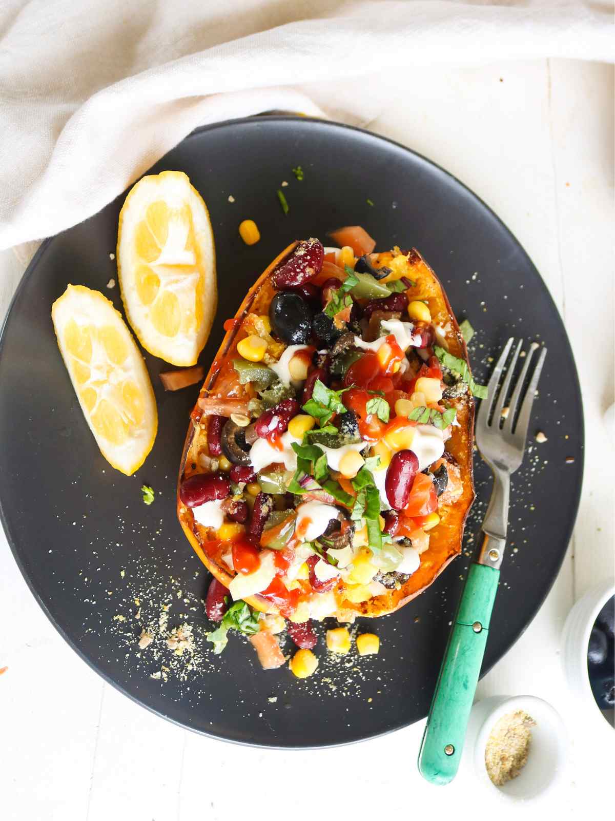 Stuffed Spaghetti Squash Served on a black plate and fork, lemon wedges placed in the background.