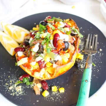 vegan stuffed spaghetti squash served on a black plate loaded with sweet corn red beans, olives, veggies and sauces.