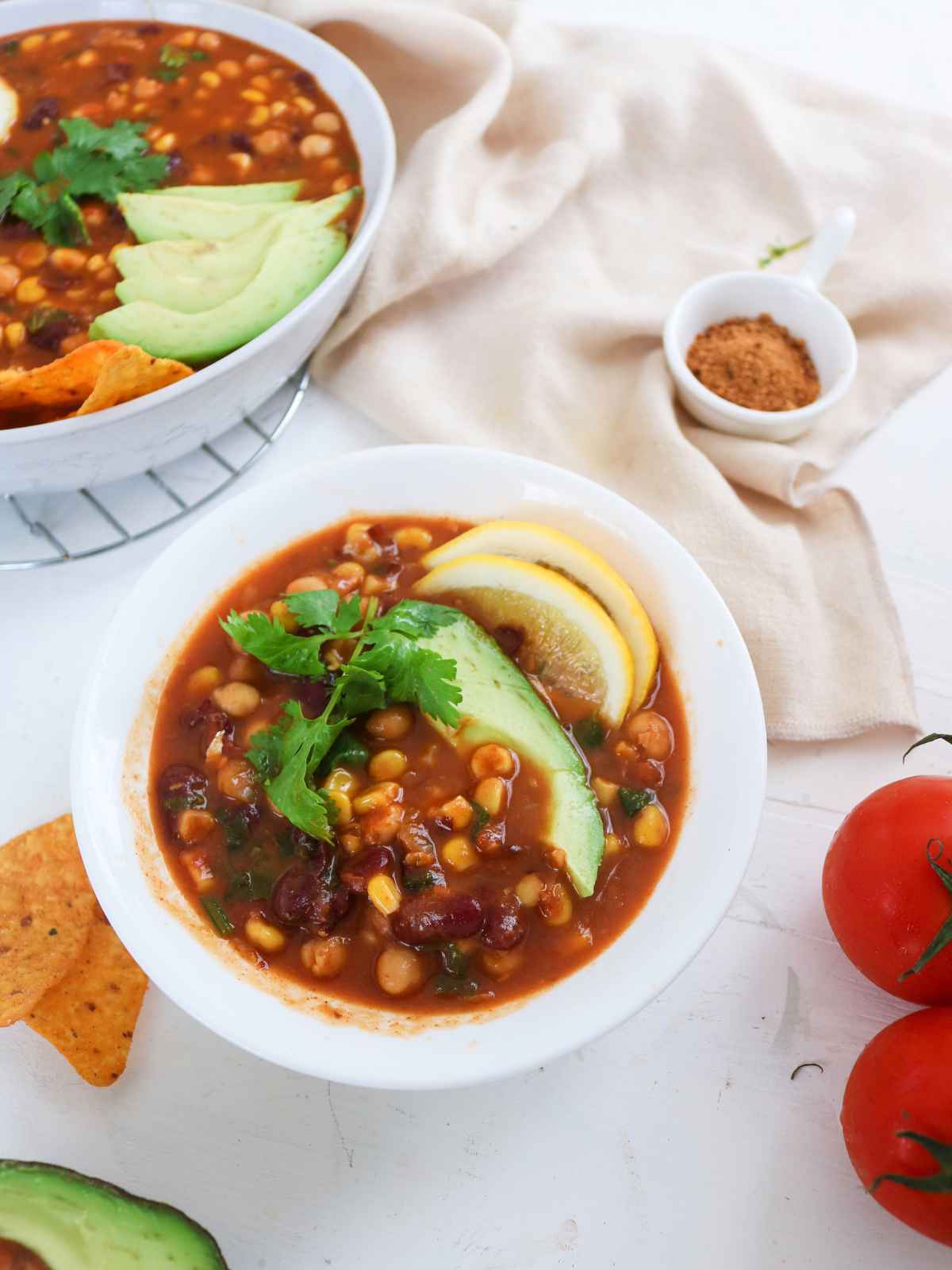 Soup served in a small bowl tomatoes and tortilla chips in background.