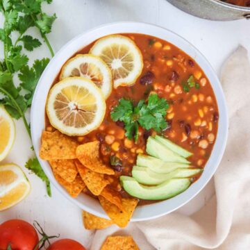 vegan taco soup served in a white bowl garnished with lemon wedges tortilla chips, avocado slices and cilantro.