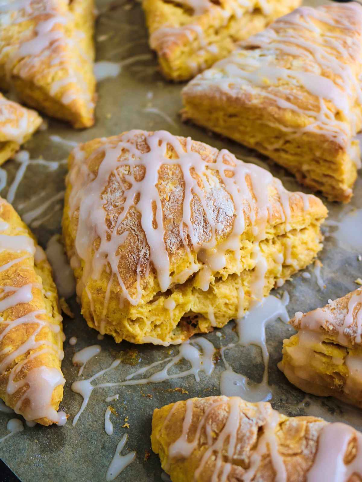 Eggless pumpkin scones on a baking tray with maple glaze drizzled on top.