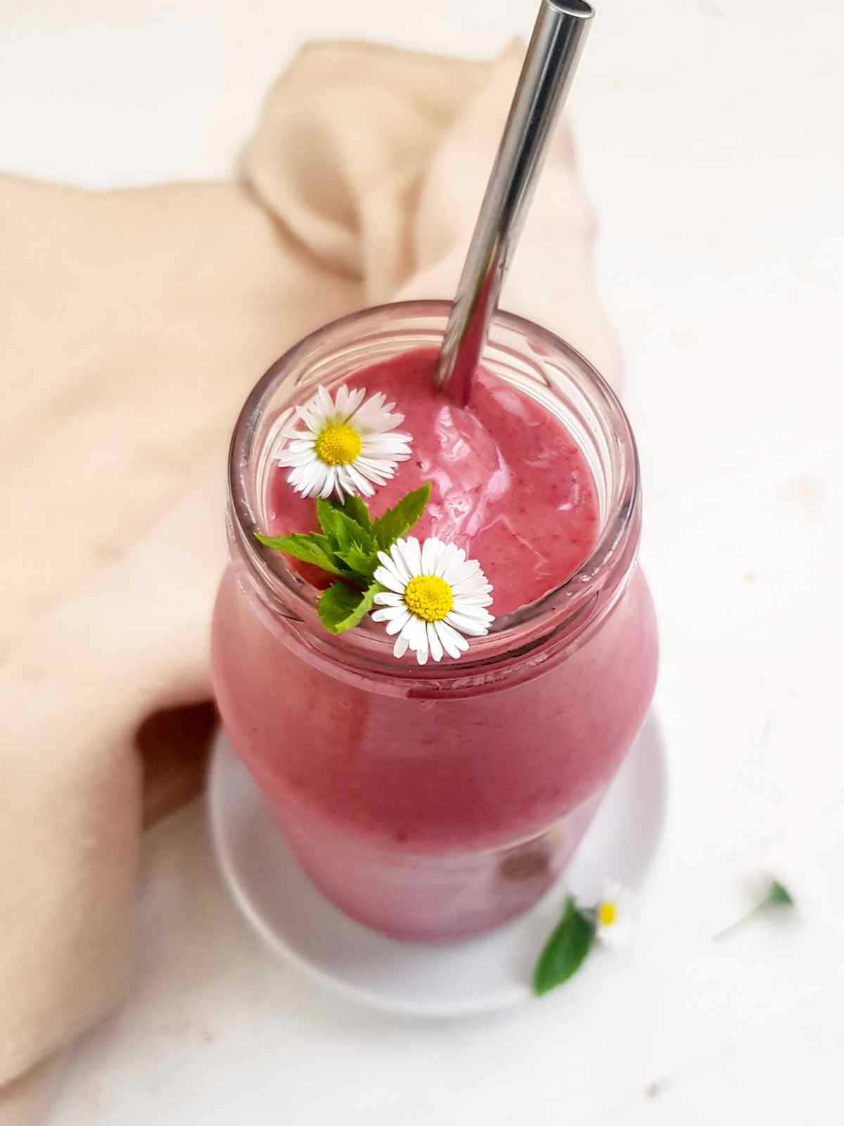 Pink color high calorie smoothie in a glass jar garnished with two white flower and mint leaf.