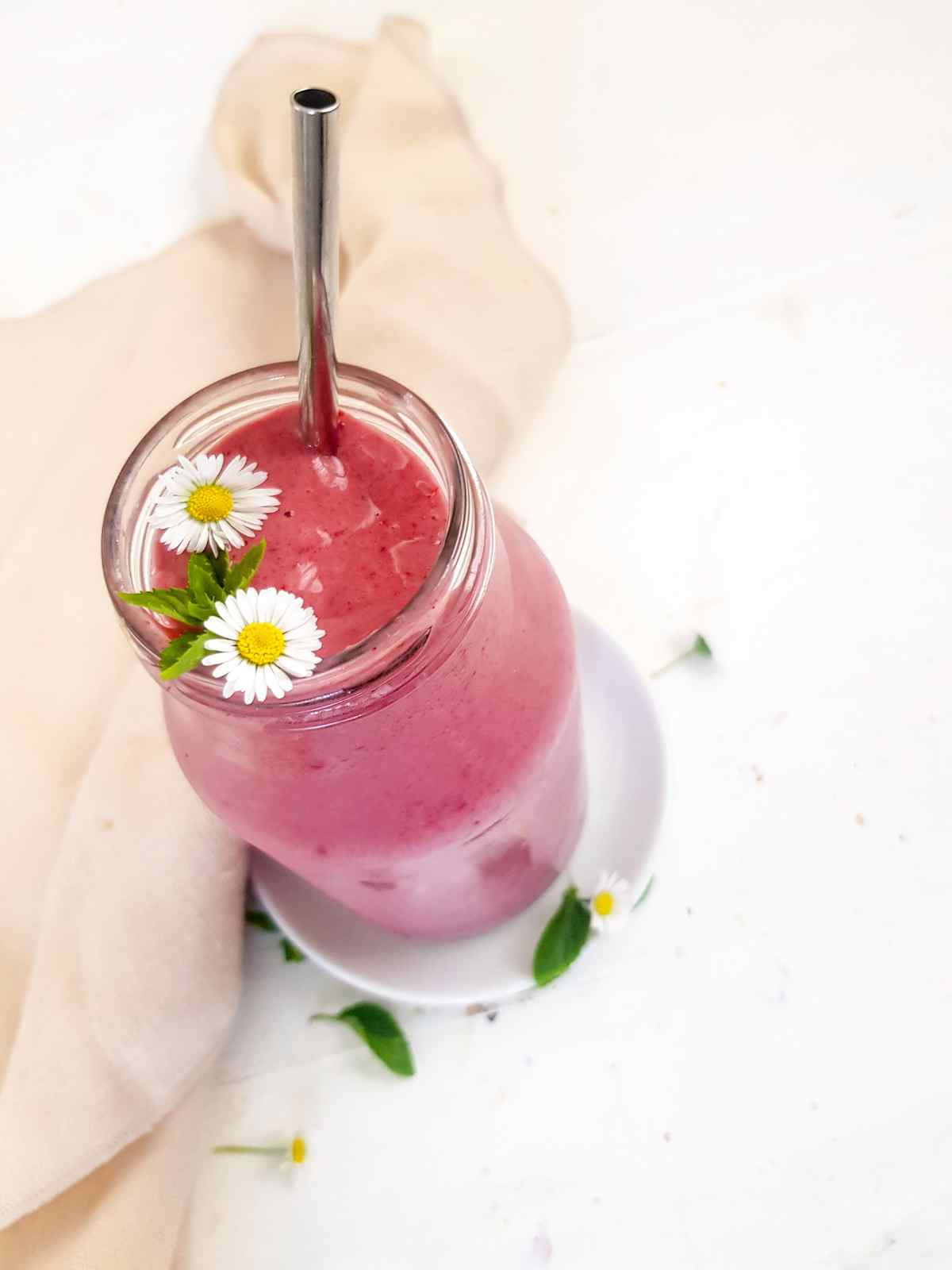 Pink color high calorie smoothie in a glass jar and a metal straw.