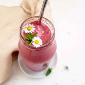 Pink color high calorie smoothie in a glass jar garnished with white flower and mint leaf.