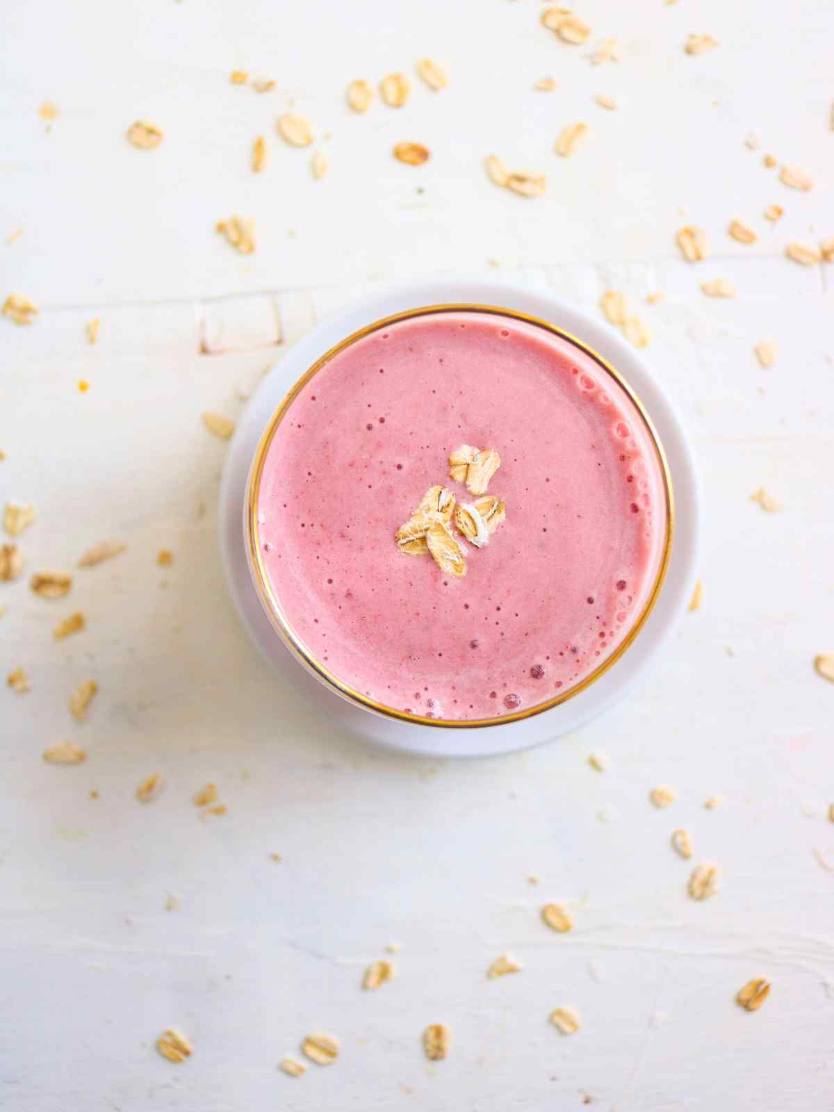 Smoothie glass placed on a white surface and oats sprinkled on background.