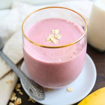 pink color oat milk smoothie served in a glass topped with some oats.