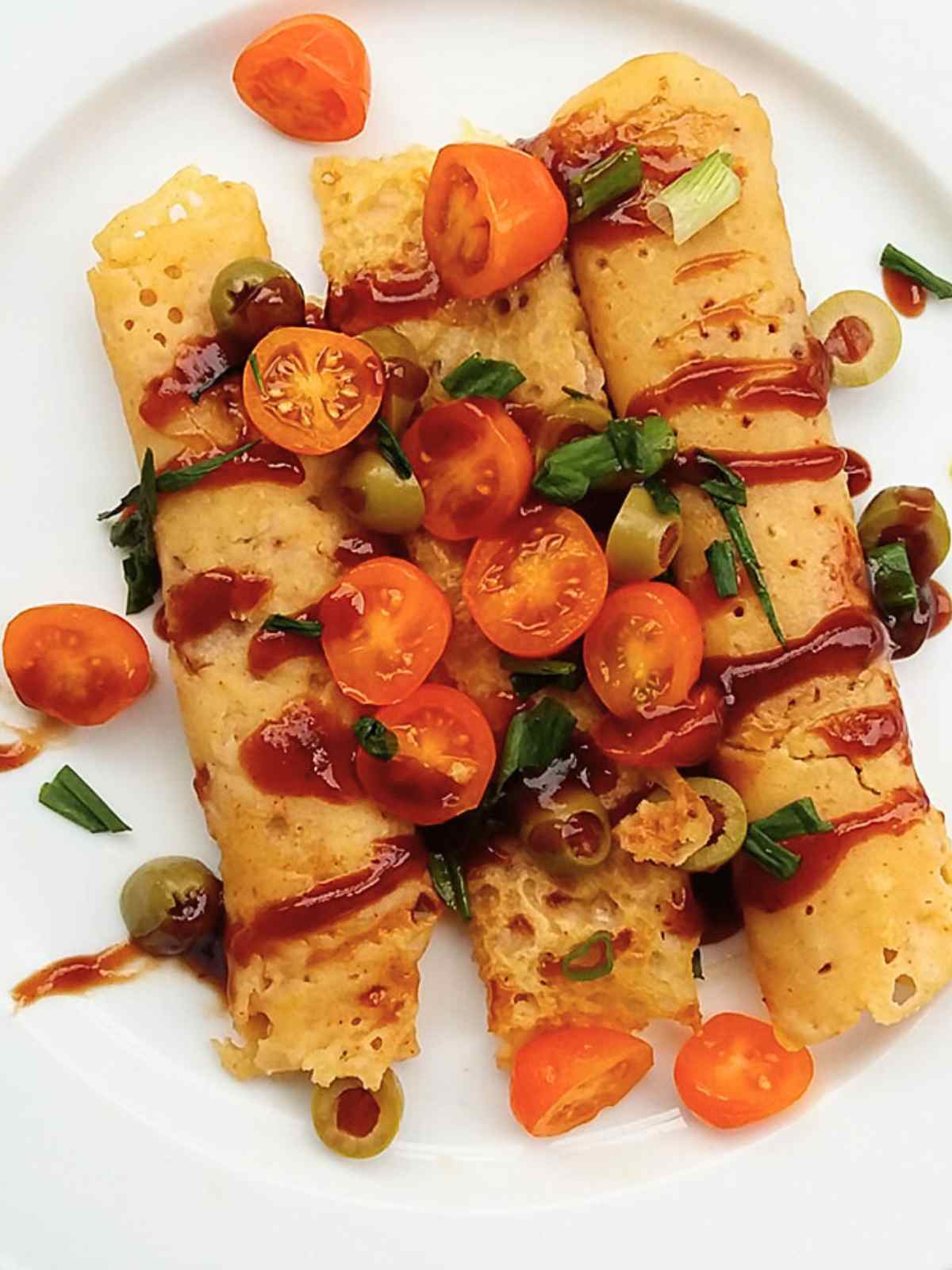 Crepes served in a white plate topped with bbq sauce, cherry tomatoes, olives and cilantro leaves. 