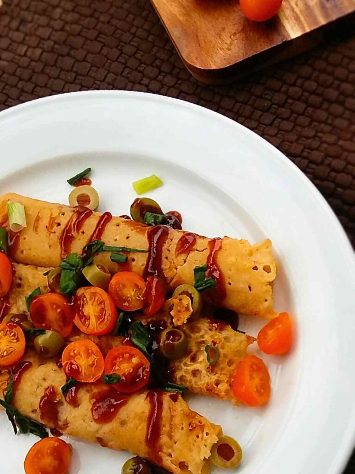 vegan savory crepes served in a white plate topped with bbq sauce, cherry tomatoes, olives and cilantro leaves. 