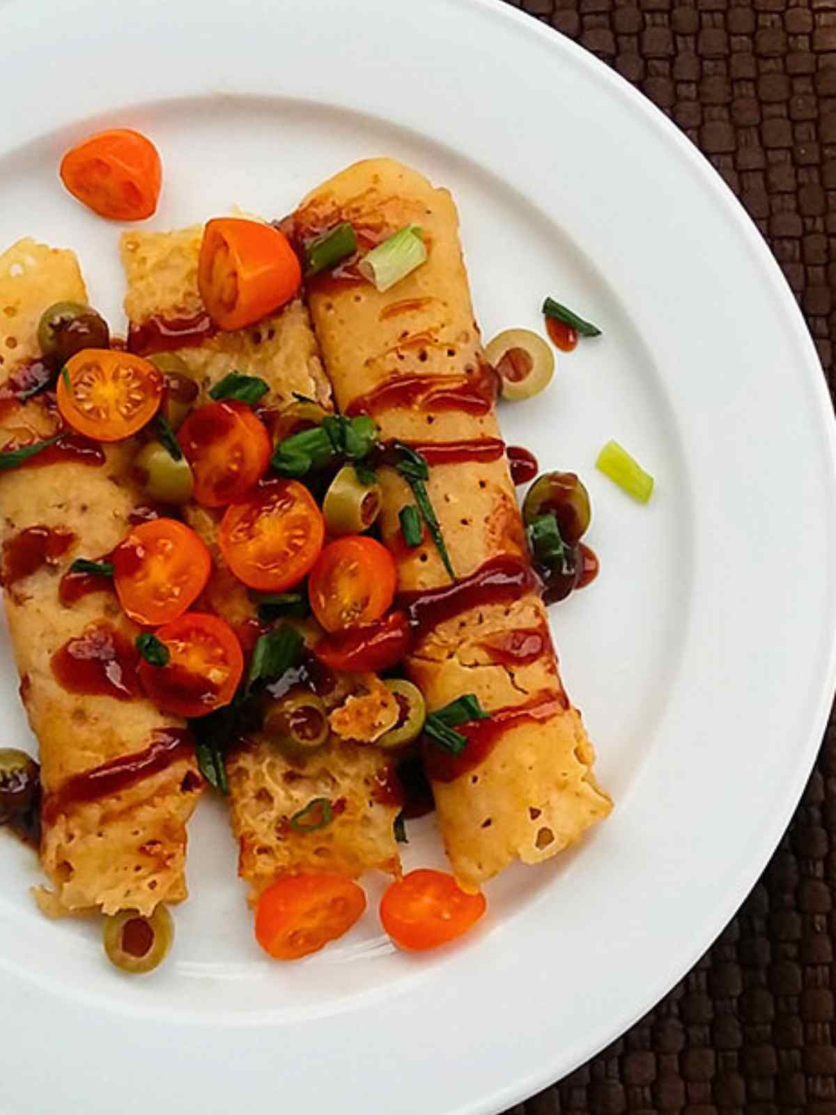 vegan savory crepes served in a white plate topped with cherry tomatoes, olives and cilantro leaves. 