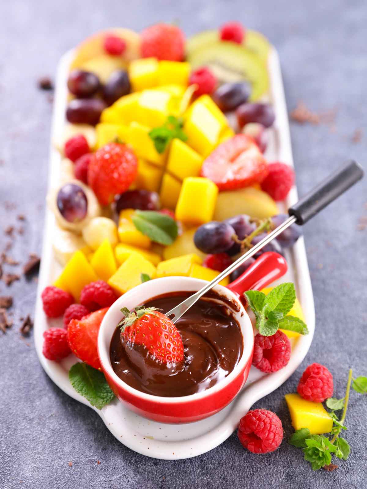 Selection of fresh fruits served on a plate with a bowl of melted chocolate. 