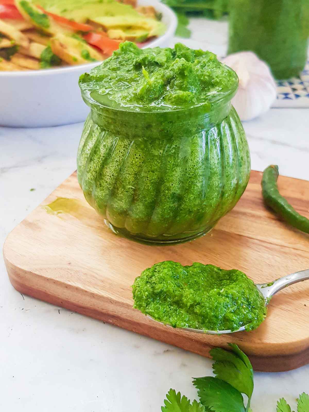 Green color coriander chutney in a glass jar and spoon.