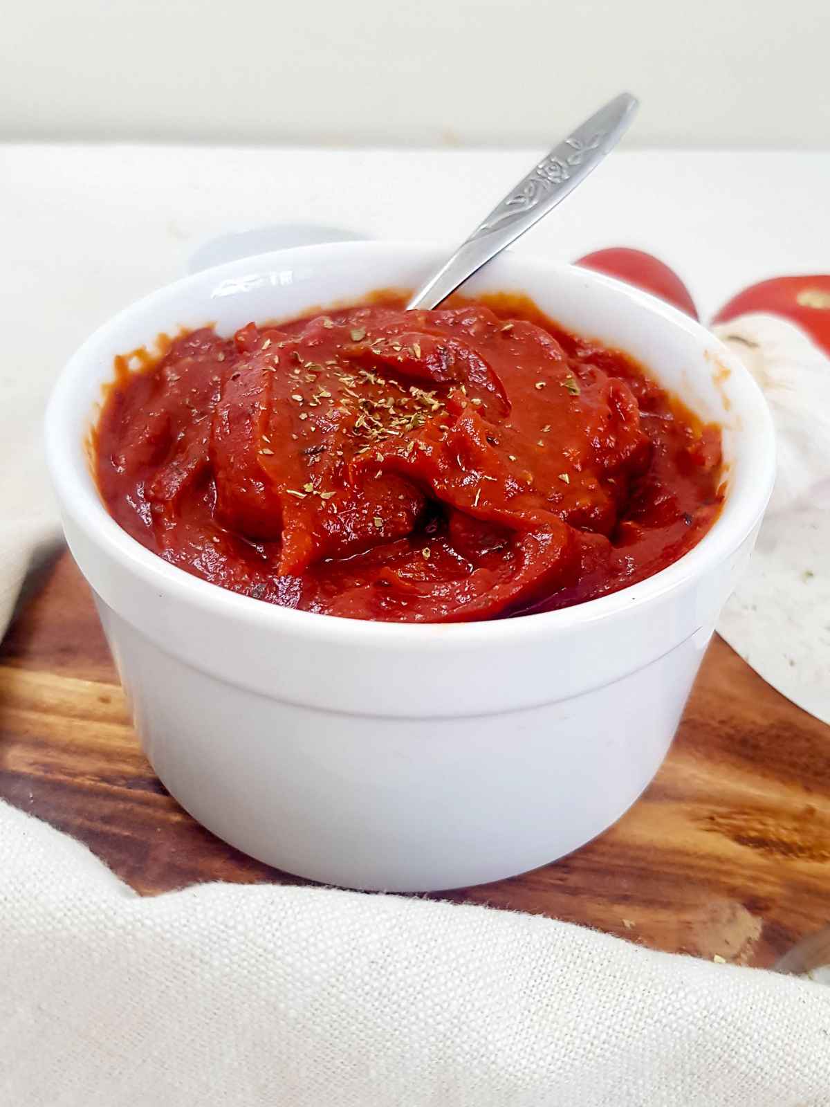 Vegan pizza sauce in a white bowl with a silver spoon on side.