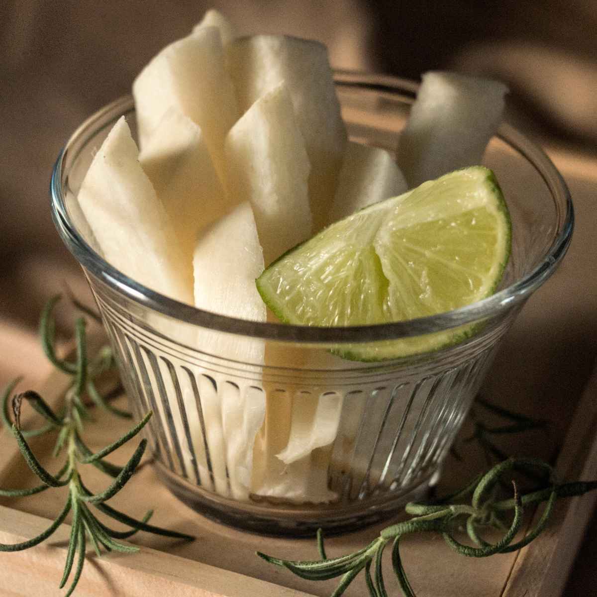 Jicama Slices placed in a glass bowl. lemon wedges on side.