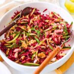 Cucumber beetroot salad served in a white bowl with wooden spoons on side.