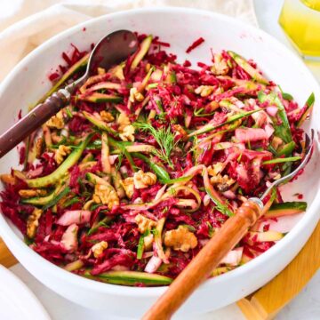Cucumber beetroot salad served in a white bowl with wooden spoons on side.