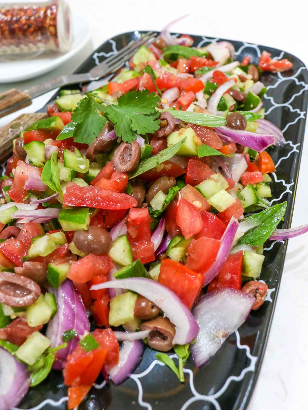 Serving colorful Mediterranean salad in black platter.