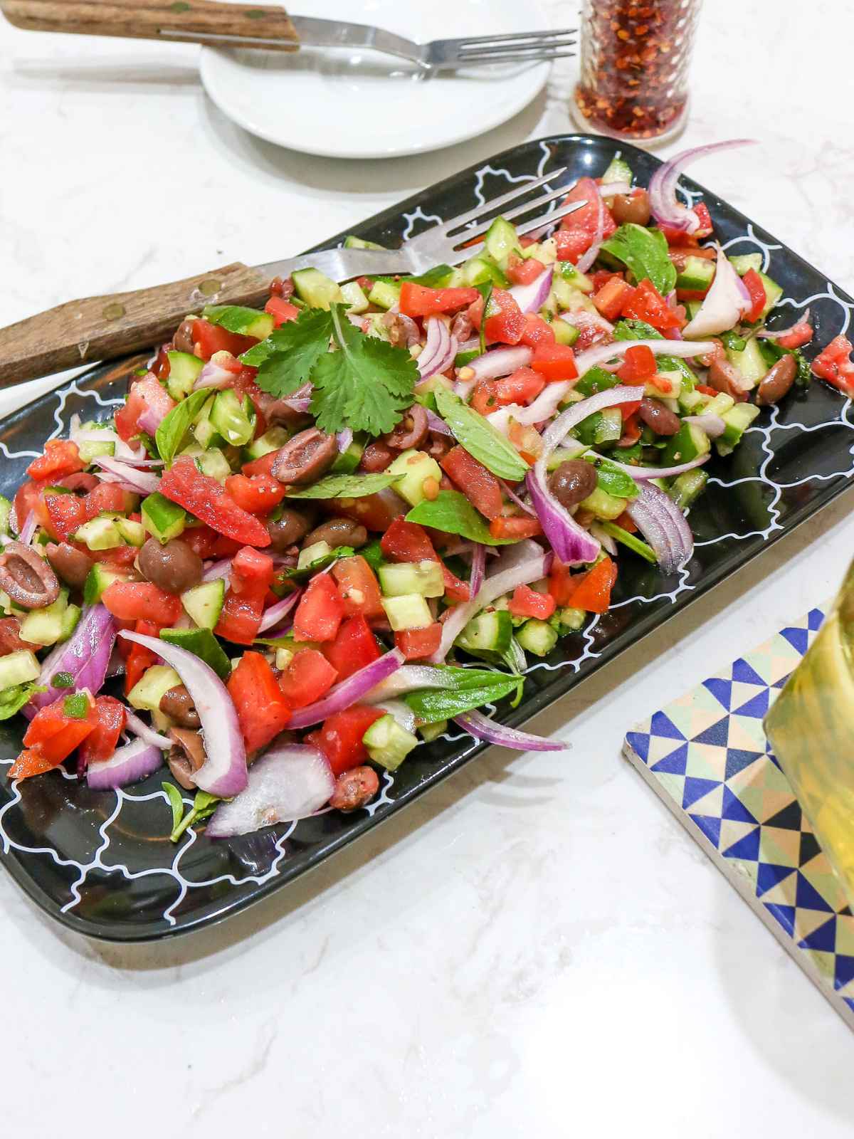 Chopped cucumber, tomatoes, onion and olives salad served in a black plate.