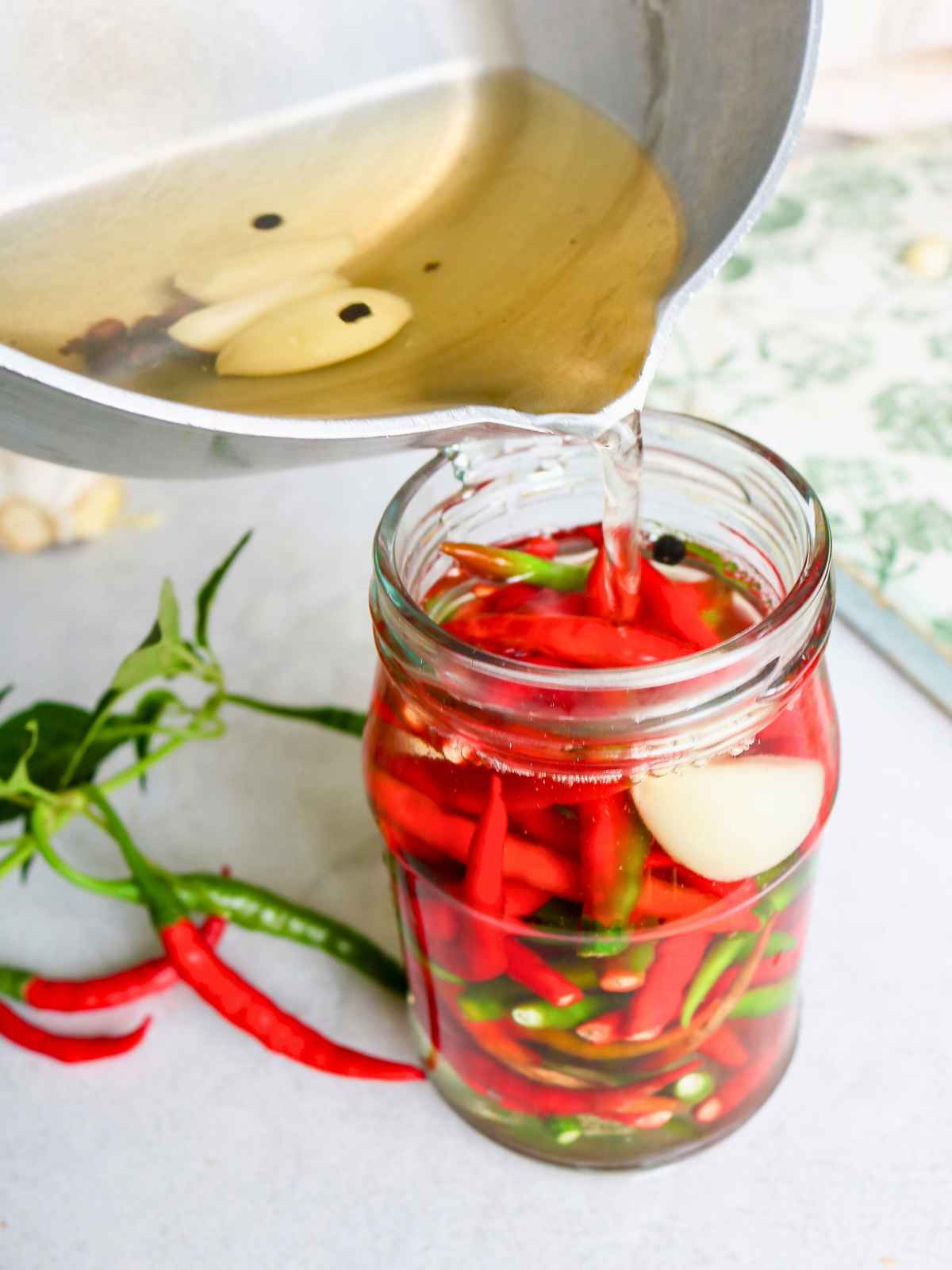 Pouring brine in a glass bottle filled with chilli peppers.