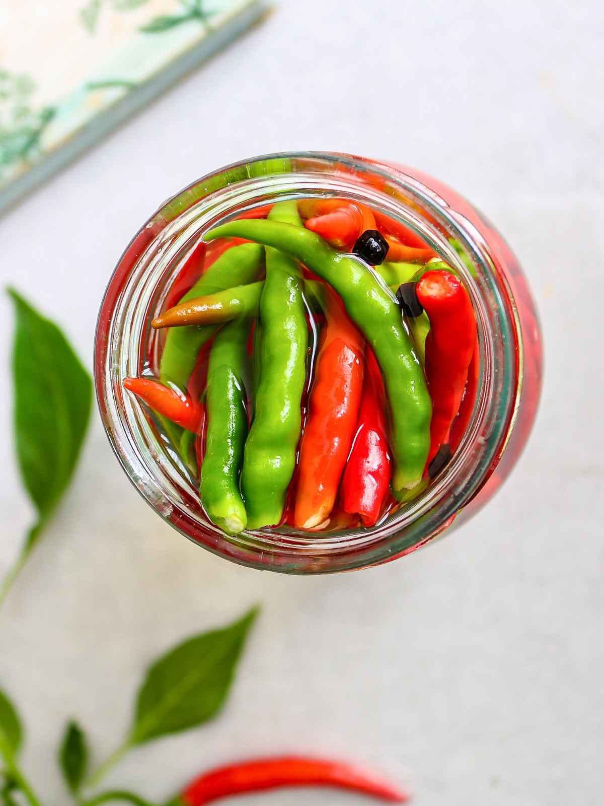 Red and green pickled chilli peppers in a glass jar.