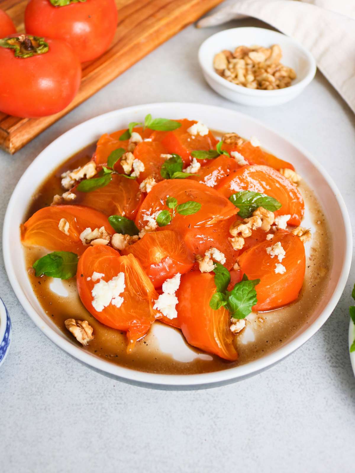 Persimmon salad served in a platter topped with mint, walnuts and cheese.