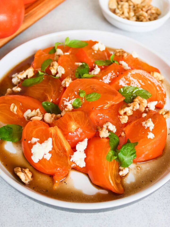 persimmon salad served in a platter topped with mint and cheese.