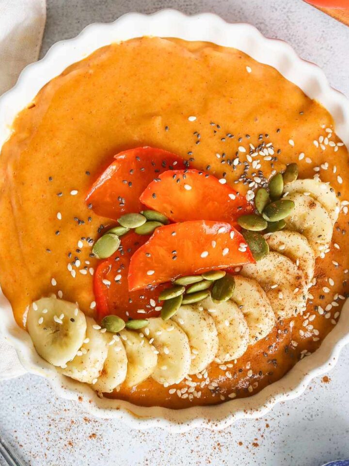 Persimmon smoothie served in a white bowl topped with fresh banana, persimmon slices and pumpkin seeds.