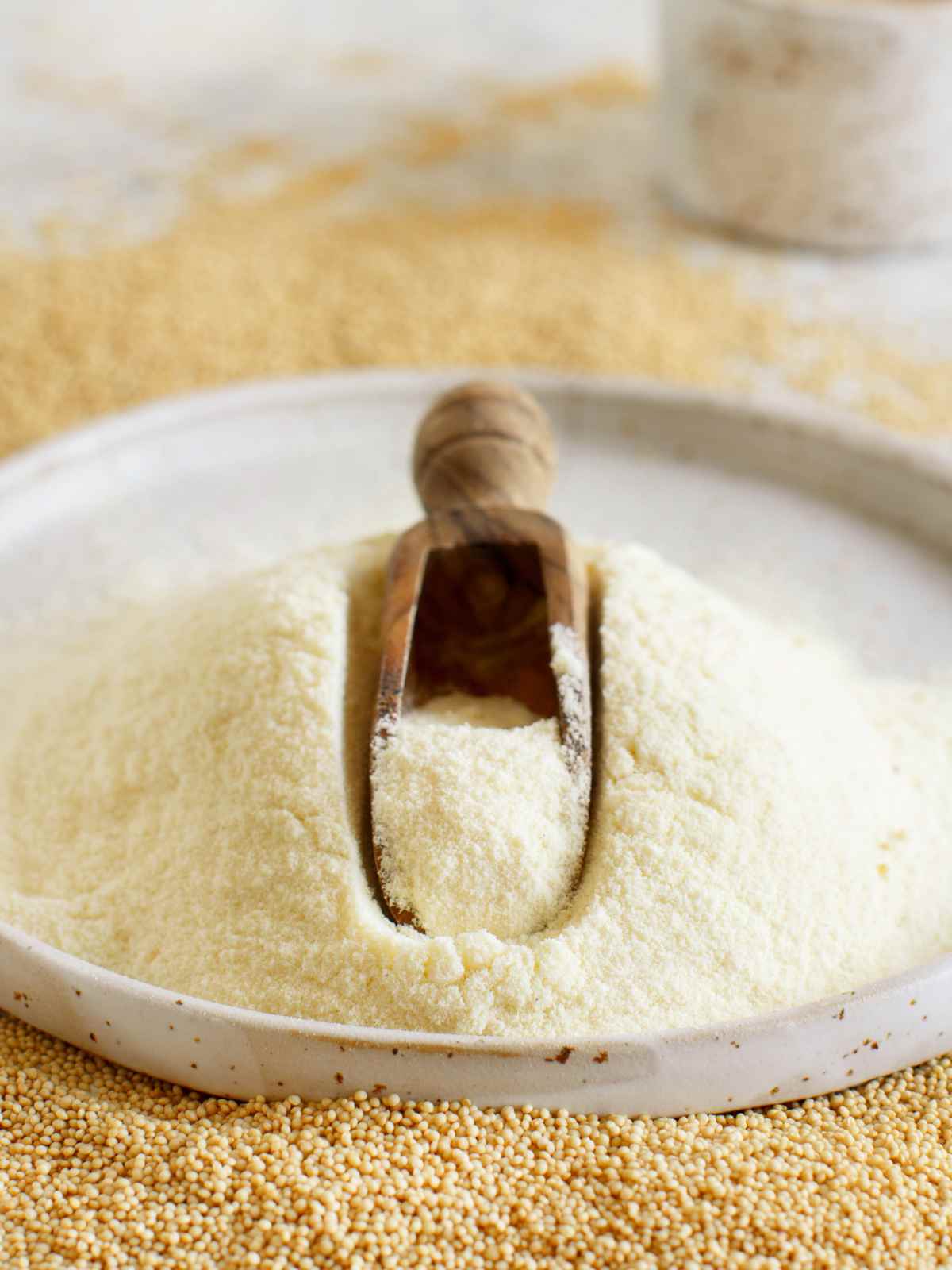 Amaranth flour is piled on a white plate, and amaranth grains are in the background.