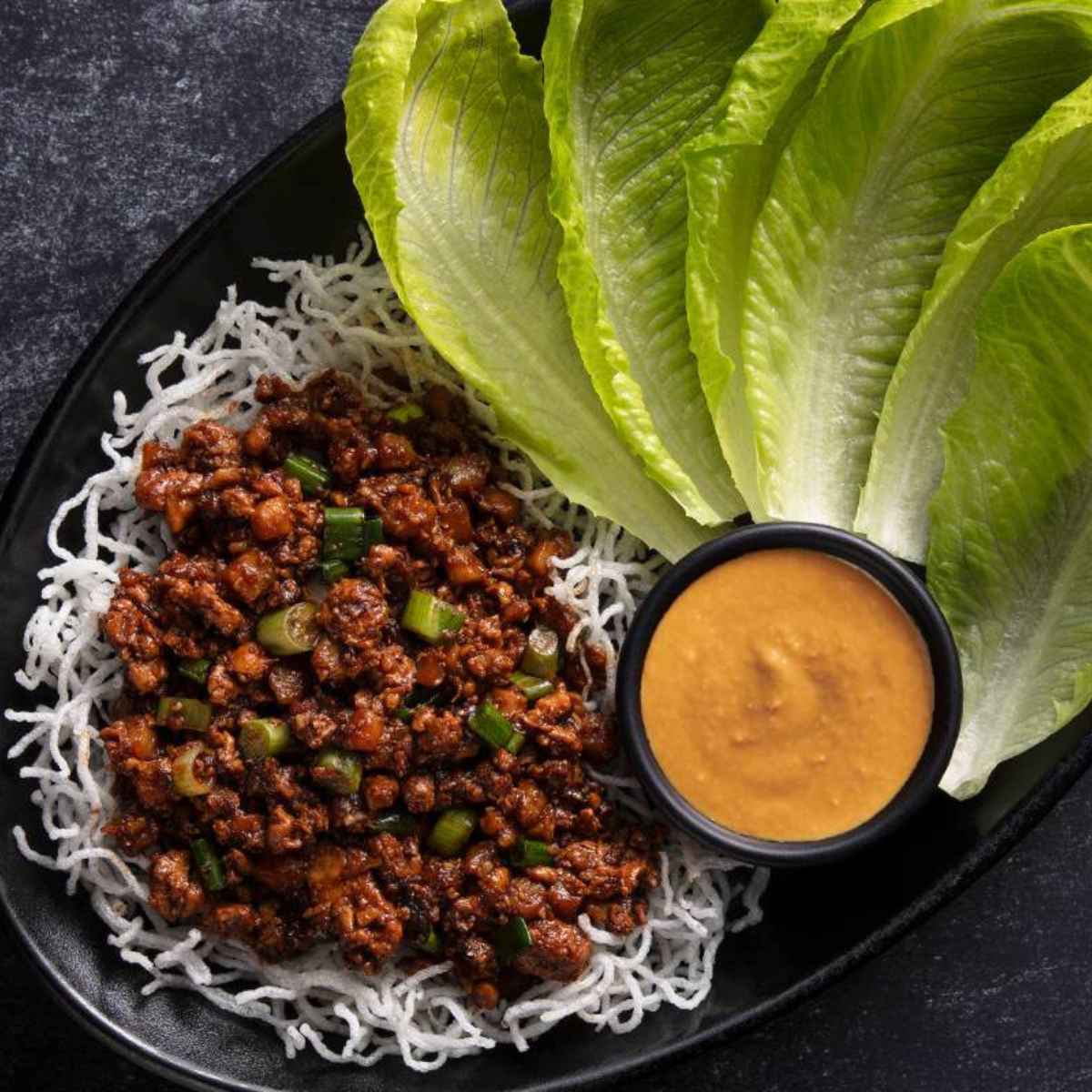 Cooked minced veggies along with crisp lettuce leaves and an orange color sauce on the side.