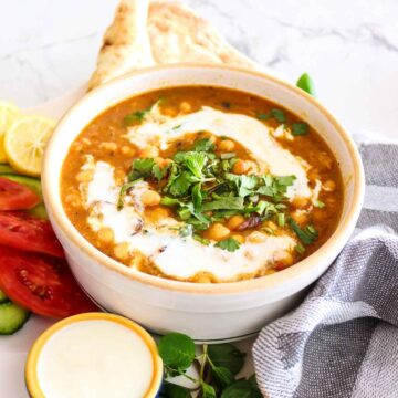 Chickpeas curry served in a white bowl topped with coconut milk and cilantro.